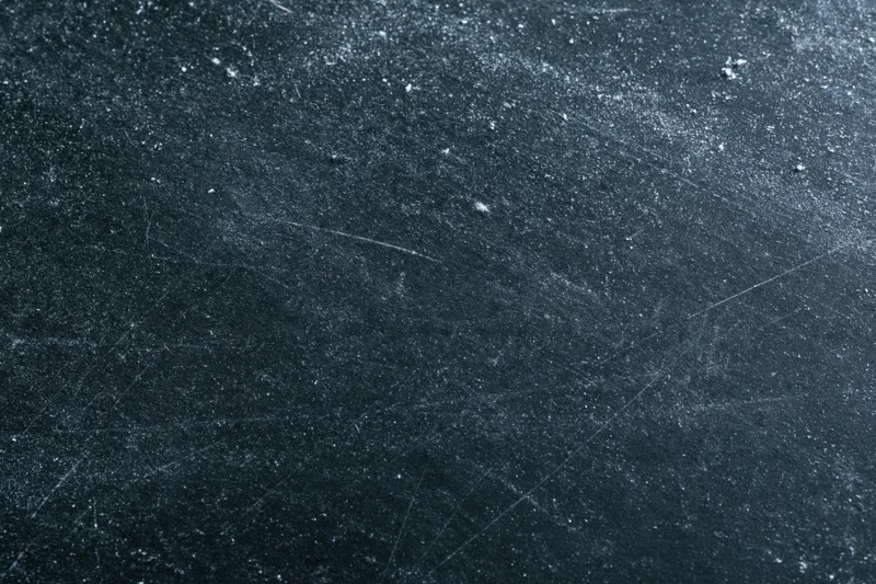 Close-up of a dark scratched chalkboard surface with dust and faint marks