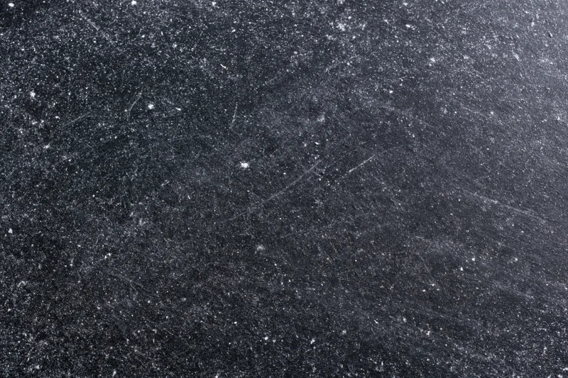 Close-up of a dark scratched chalkboard surface with white specks and marks