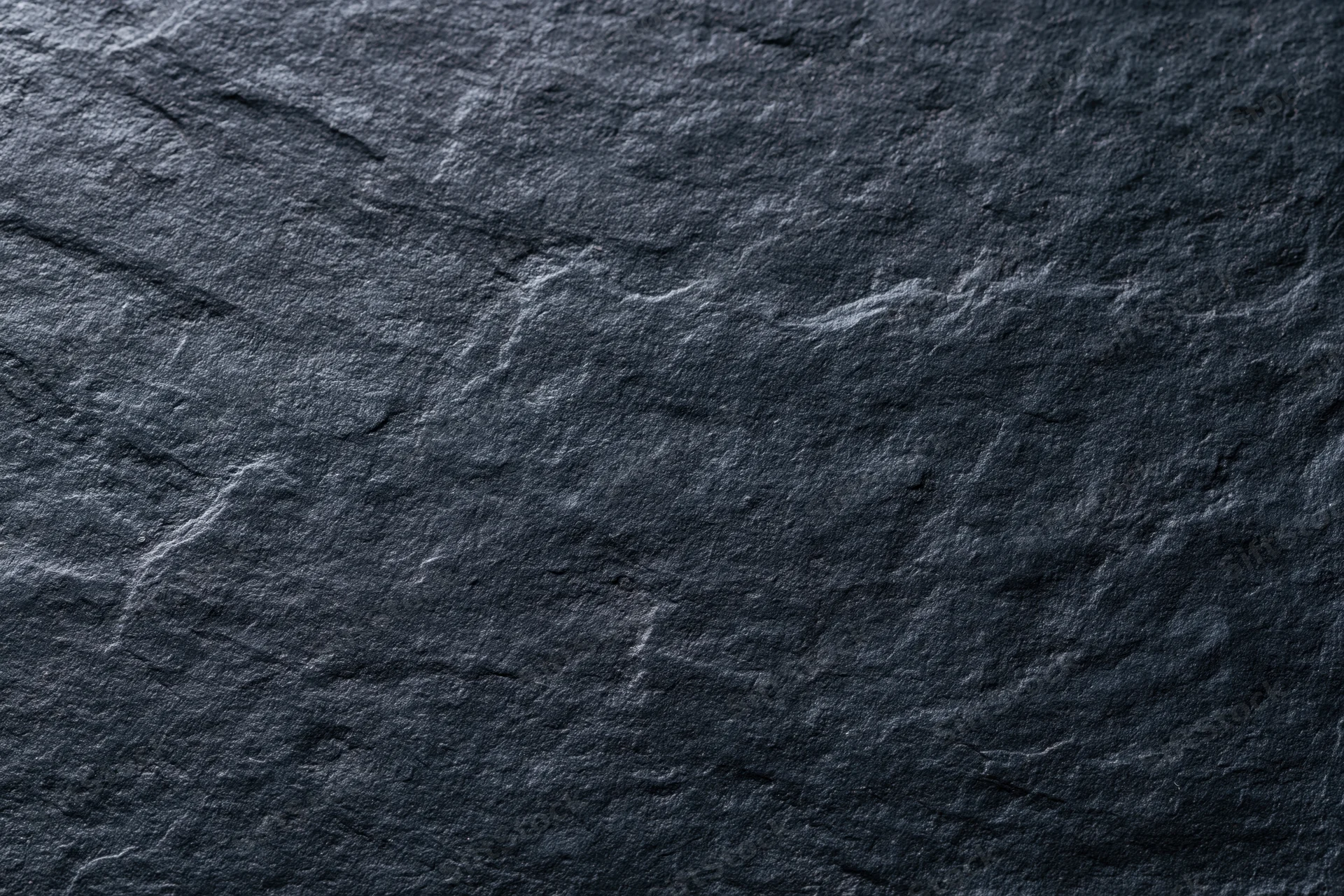 Close-up of dark slate stone surface with natural texture and grain filling the frame