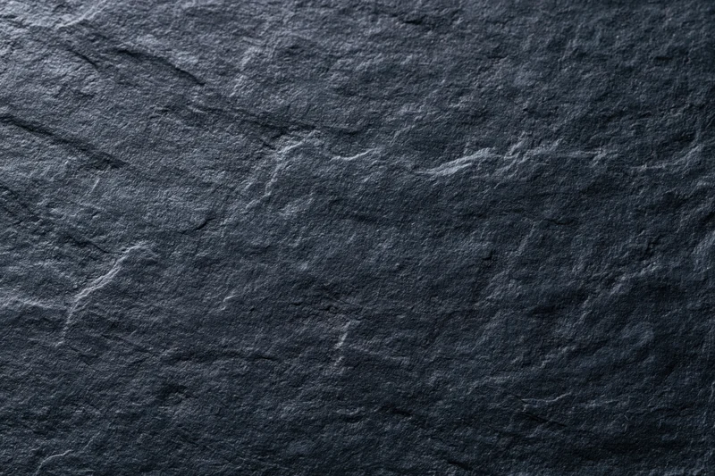 Close-up of dark slate stone surface with natural texture and grain filling the frame