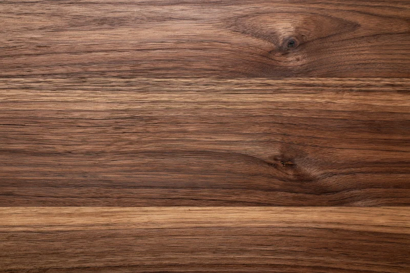 Close-up of dark walnut wood surface with visible grain and knots, flat lay view