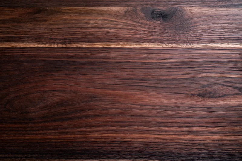 Close-up of dark walnut wood surface with visible grain and knots filling the frame