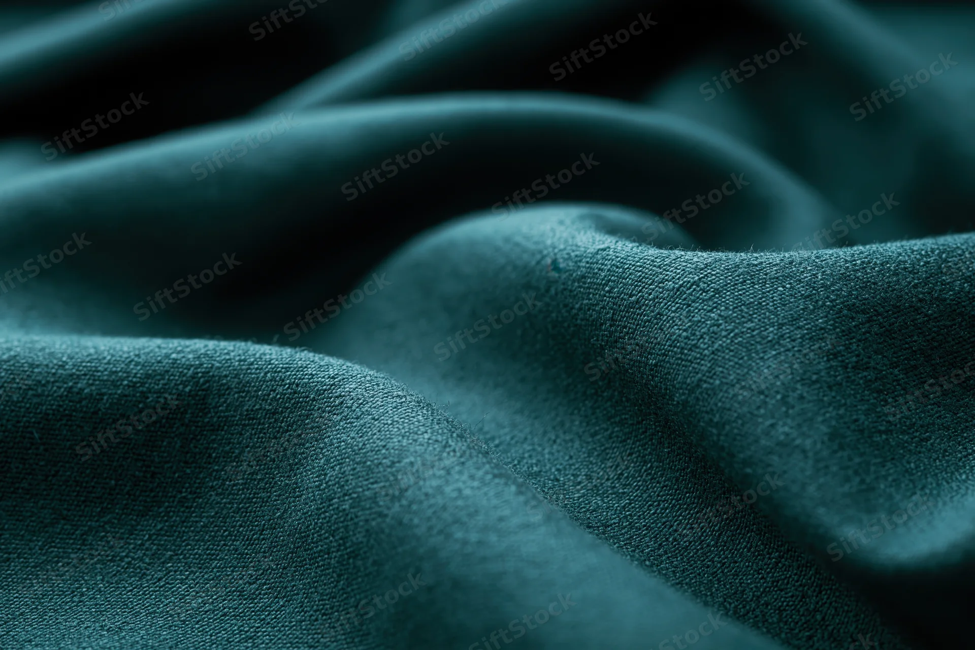 Close-up of deep teal-green fabric with soft folds and visible weave texture filling the frame