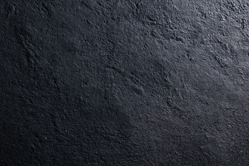 Close-up of dark charcoal concrete wall surface with rough texture and subtle lighting variation