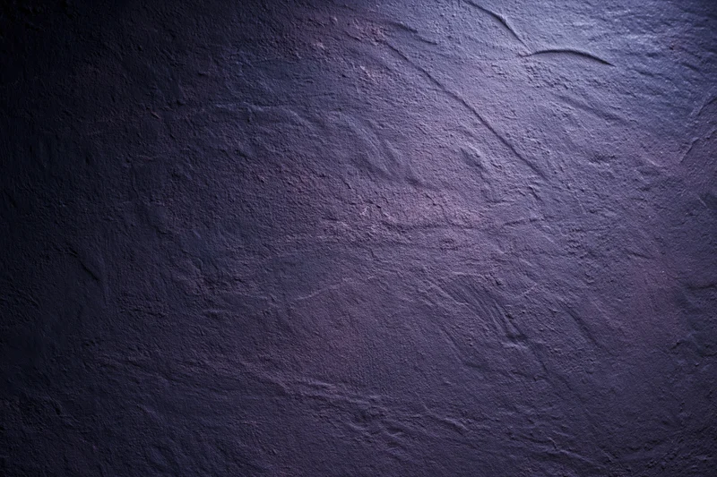 Close-up of rough plastered wall surface with dark purple and blue tones