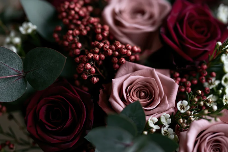 Close-up of a dense floral arrangement with dusty pink and burgundy roses, eucalyptus leaves, and small white flowers