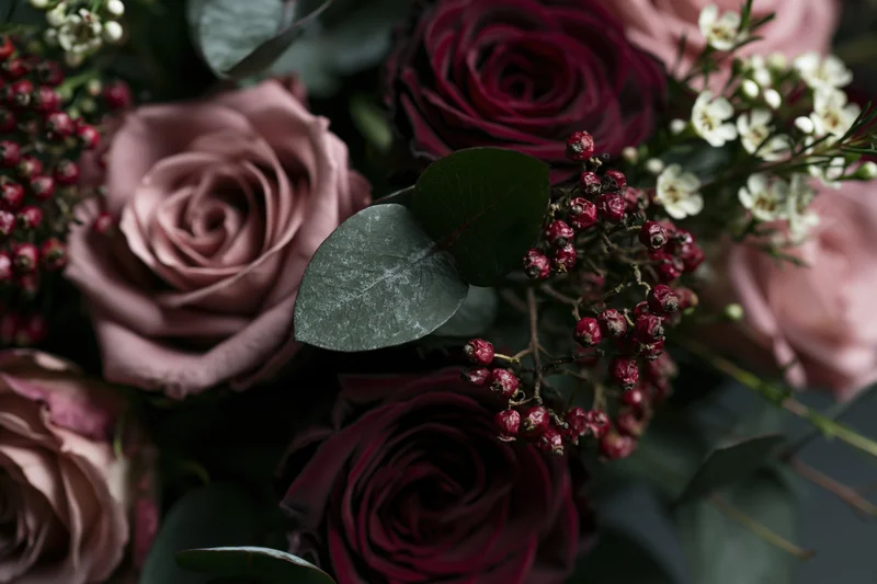 Close-up of a dense floral arrangement with dusty pink and burgundy roses, eucalyptus leaves, and red berries