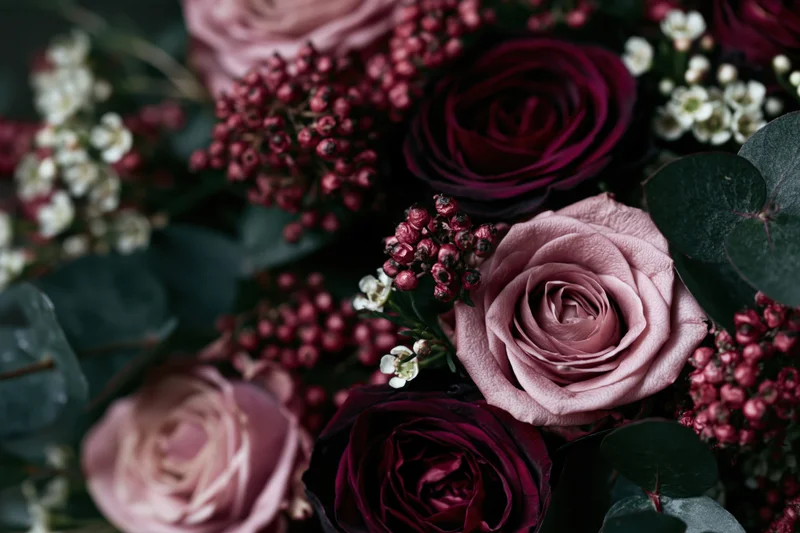 Close-up of a dense floral arrangement with dusty pink and deep burgundy roses, eucalyptus leaves, and red berries