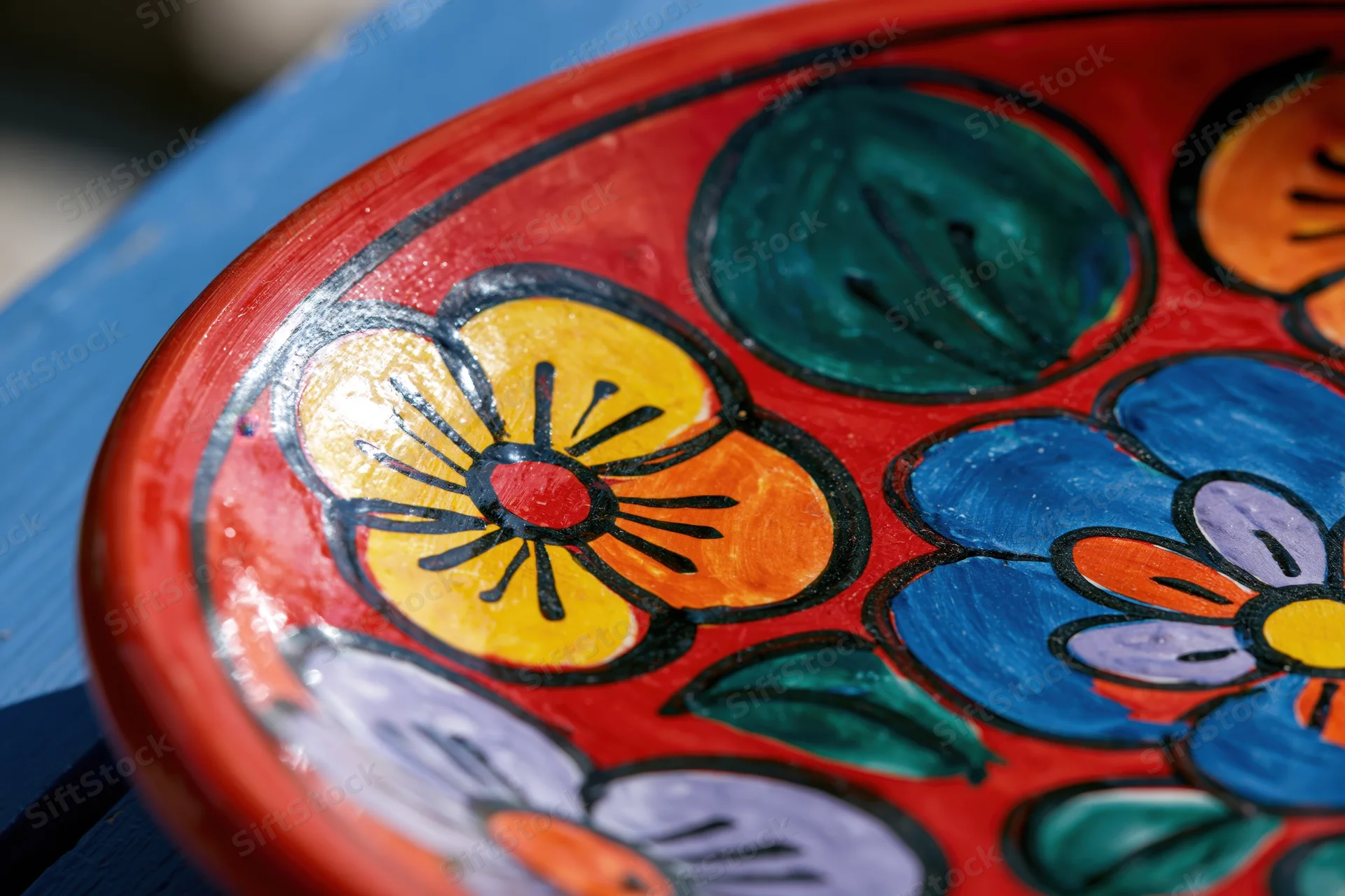 Close-up of a hand-painted mexican talavera ceramic plate with colorful floral design on red background