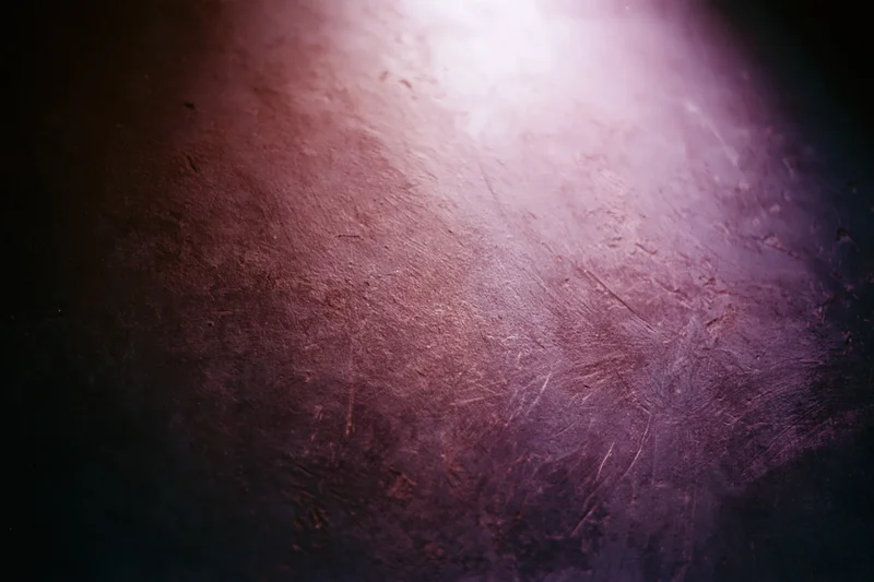 Close-up of a worn concrete wall surface with purple and pink lighting and visible scratches