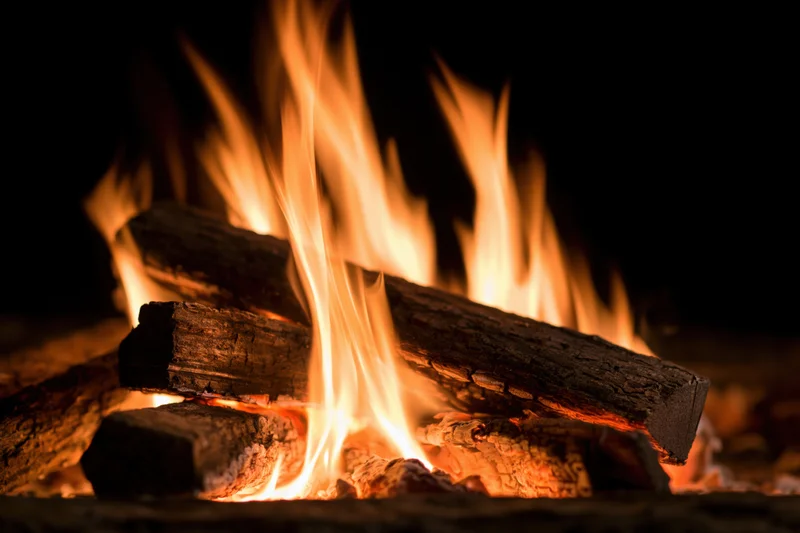 Burning wood logs with tall orange and yellow flames in a dark setting