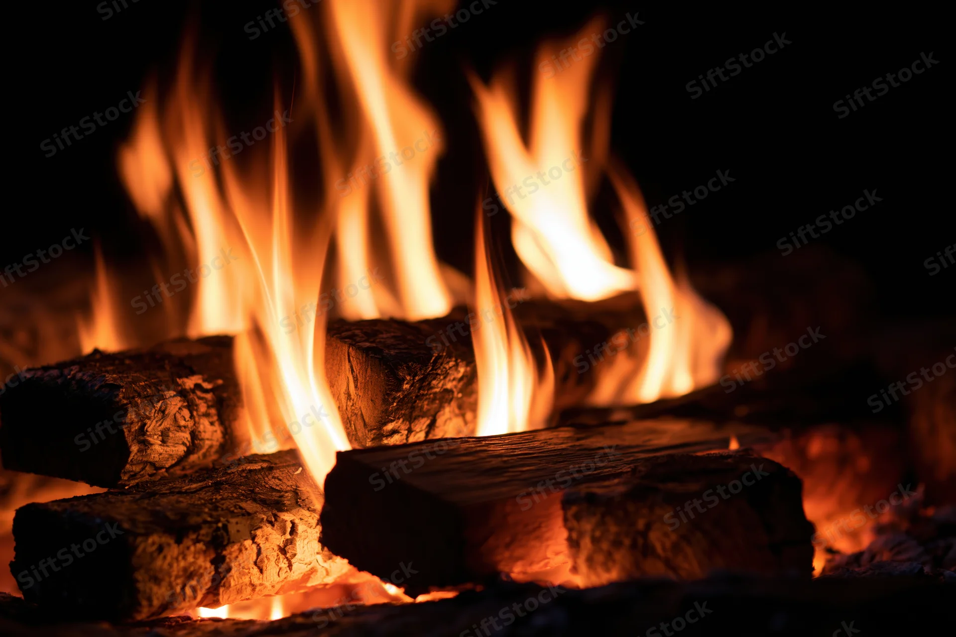 Close-up of burning wood logs with tall orange and yellow flames in a dark setting