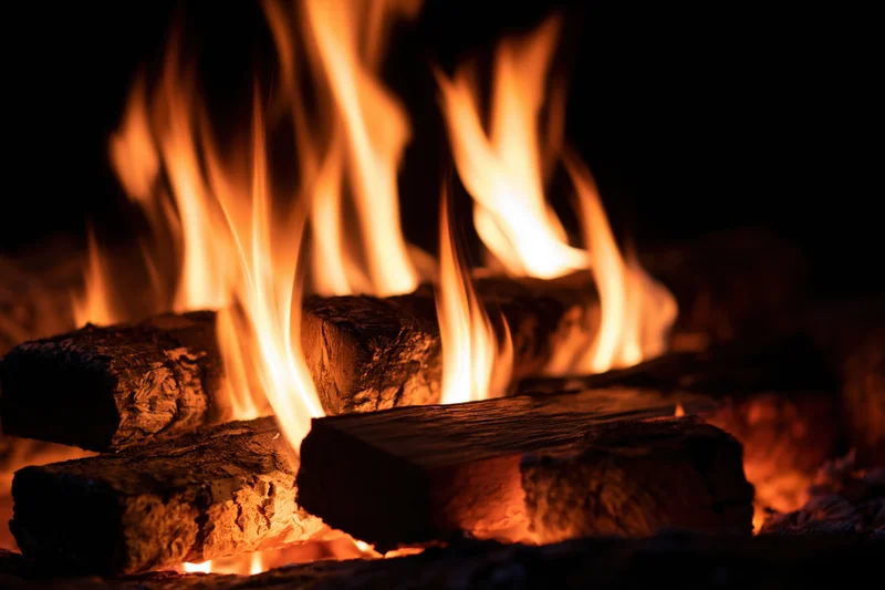 Close-up of burning wood logs with tall orange and yellow flames in a dark setting