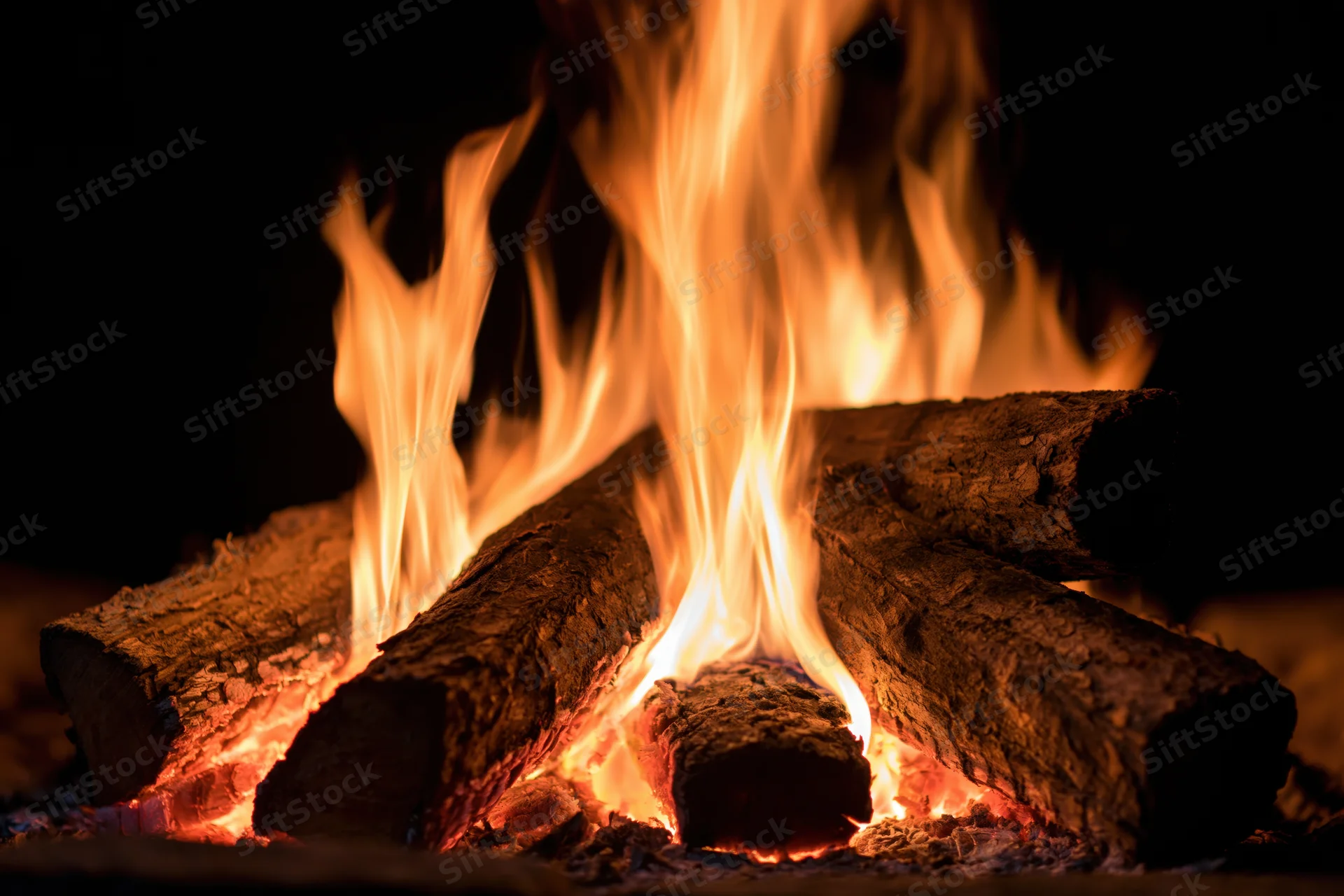 Burning wood logs with tall orange and yellow flames in a dark setting