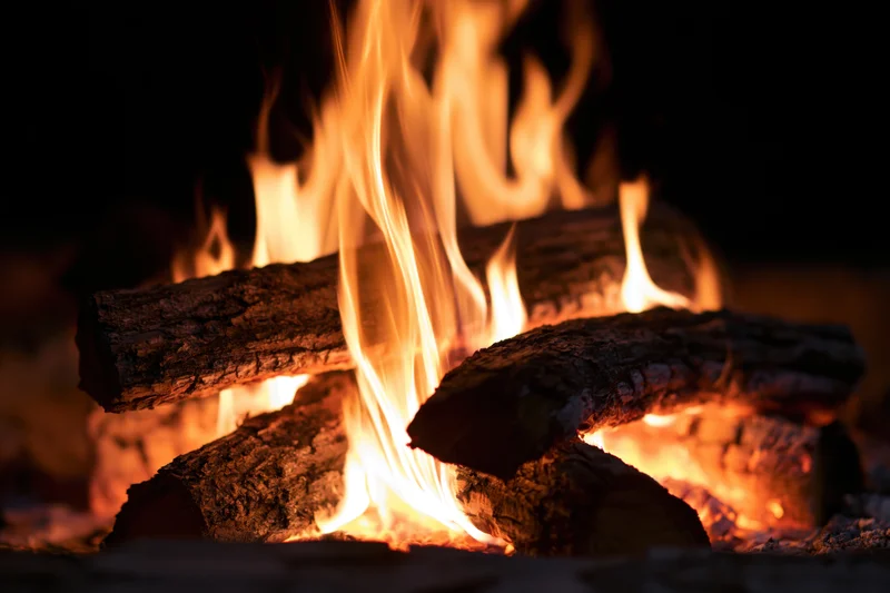 Close-up of burning wood logs with tall orange and yellow flames in a dark setting