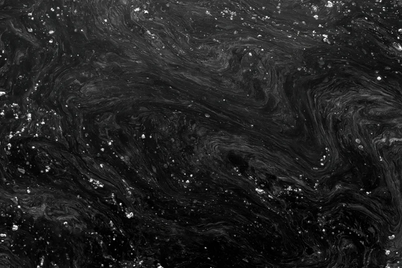 Swirling dark oily water surface with reflective sheen and scattered droplets