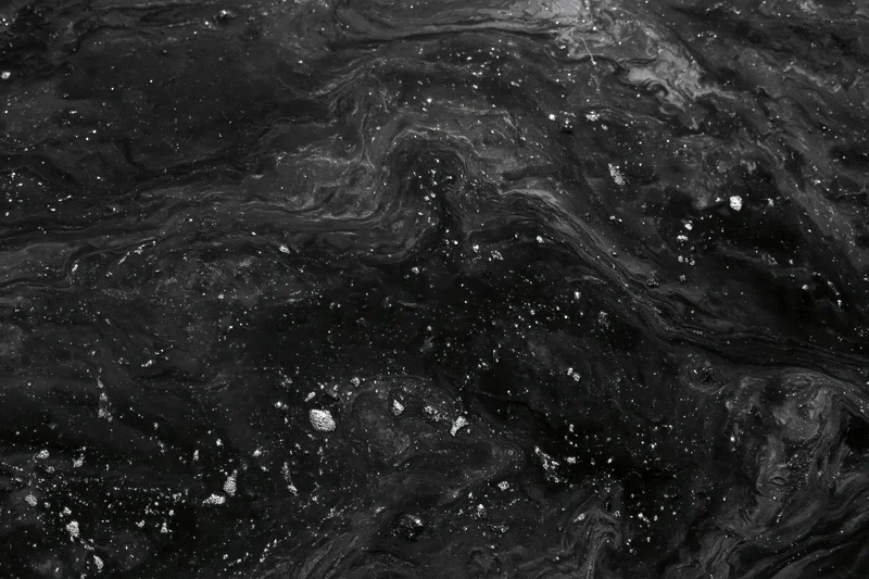 Dark oily water surface with swirling patterns and scattered bubbles