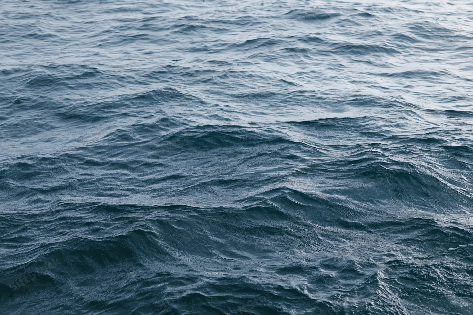 Overhead closeup of rolling ocean waves with textured surface and subtle light reflections