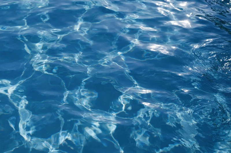 Rippling surface of clear blue pool water reflecting sunlight overhead