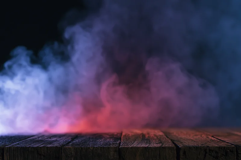 Colored smoke rising from a wooden table surface against dark background
