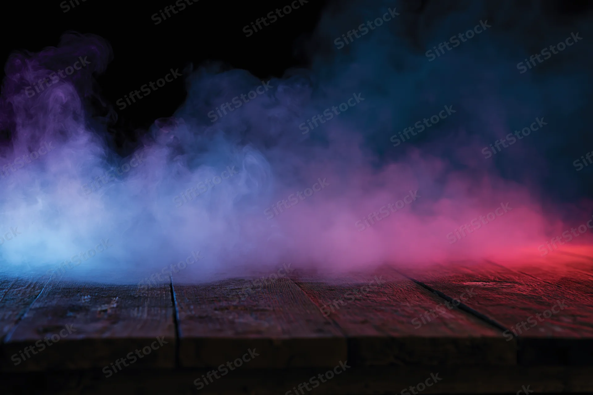 Colored smoke rising from a wooden surface against a dark background
