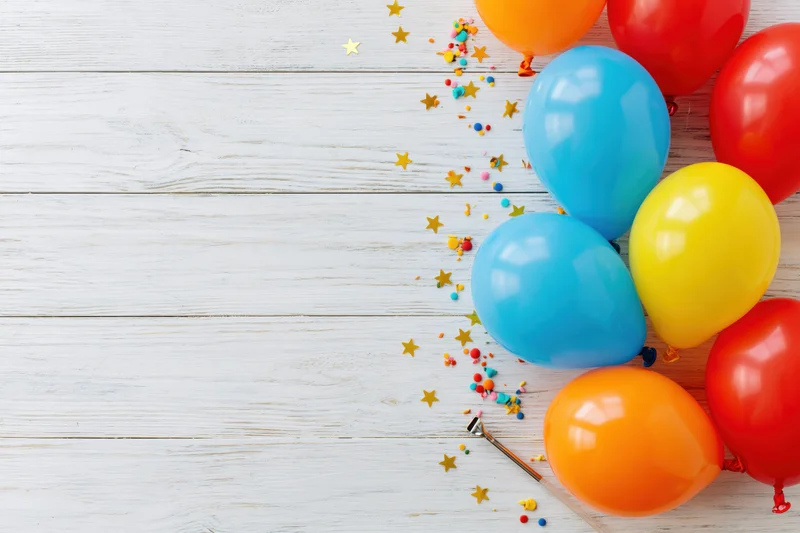 Colorful latex balloons and confetti arranged on white wooden surface with copyspace