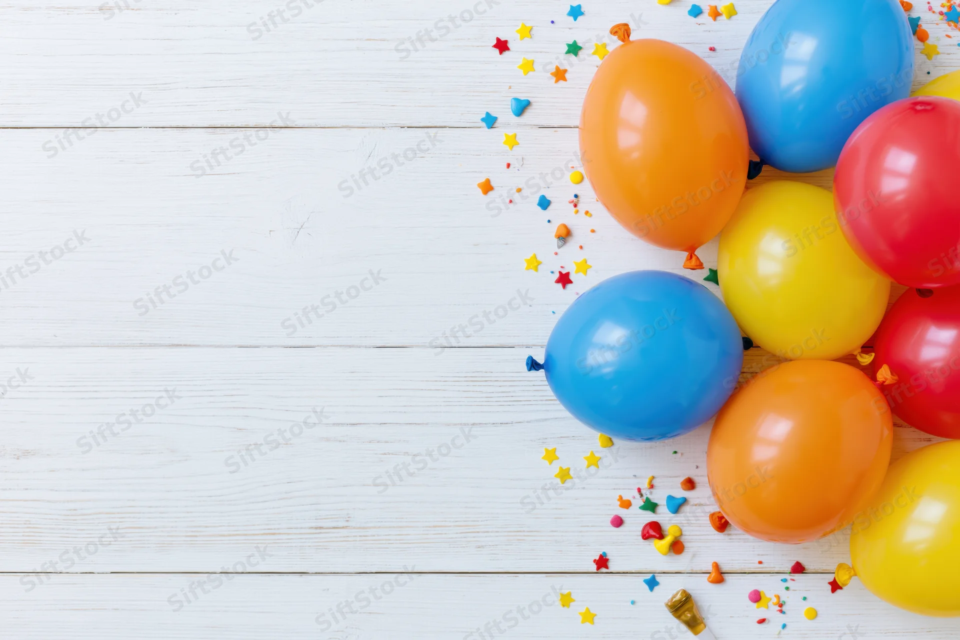 Colorful latex balloons and confetti clustered on white wooden surface