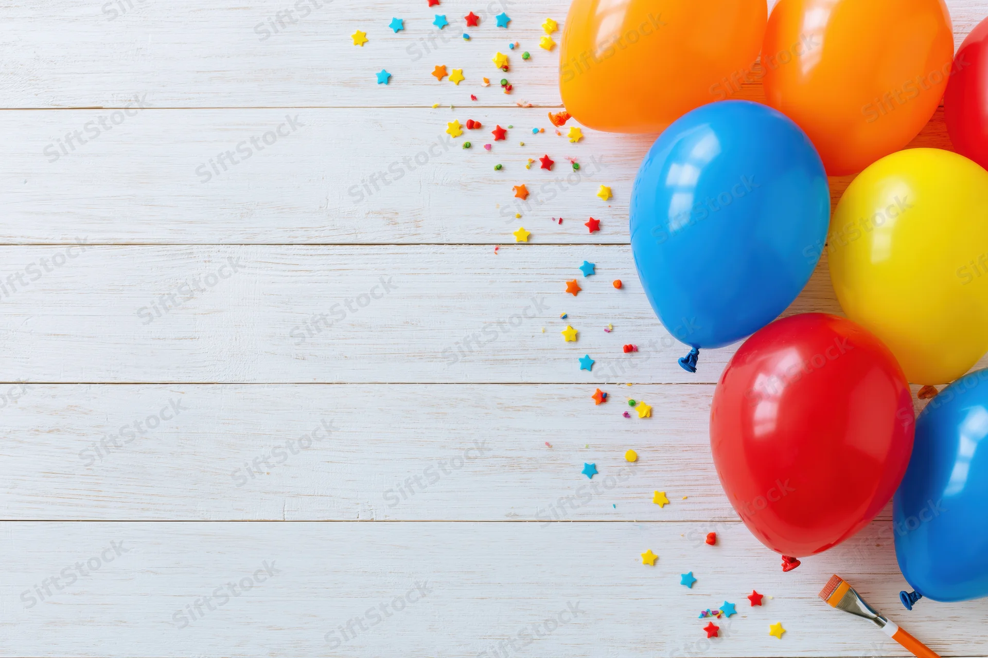 Colorful latex balloons and star-shaped confetti arranged on a white wooden surface