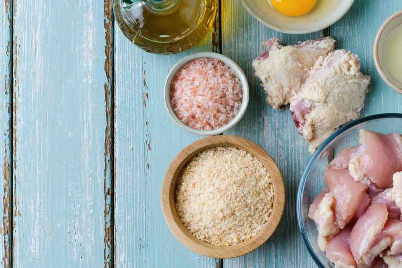 Raw chicken pieces and cooking ingredients arranged in bowls on a weathered blue wooden surface
