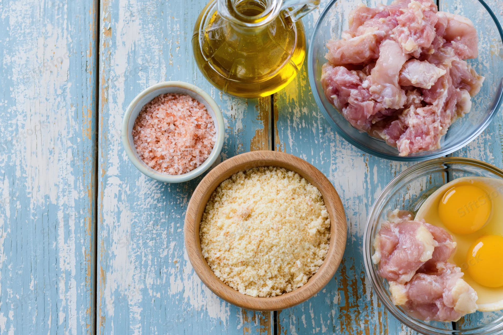 Raw chicken pieces and cooking ingredients arranged in bowls on a weathered blue wooden surface