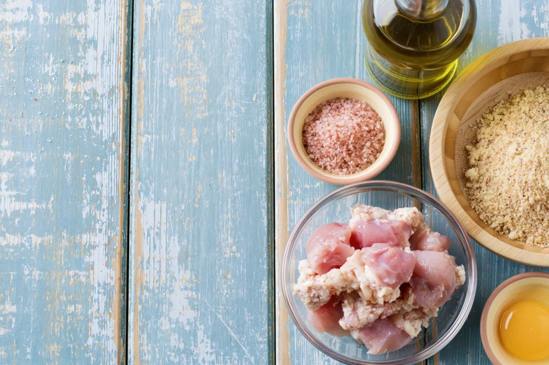 Raw chicken pieces and cooking ingredients arranged on a weathered blue wooden table in a flat lay composition