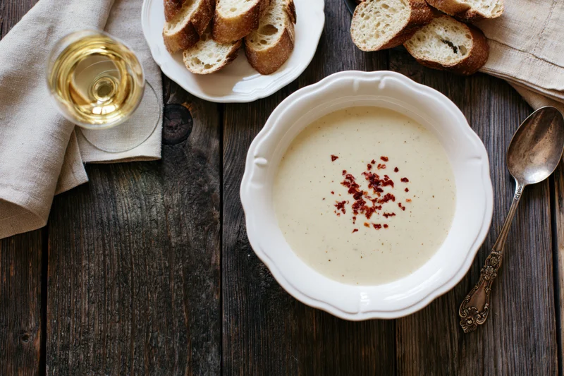 Cream soup with red pepper flakes in a white vintage bowl on a dark wooden table with bread and wine