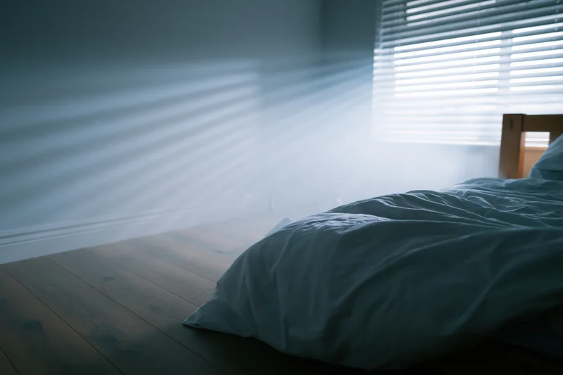 Unmade bed with wooden frame in dark bedroom at night