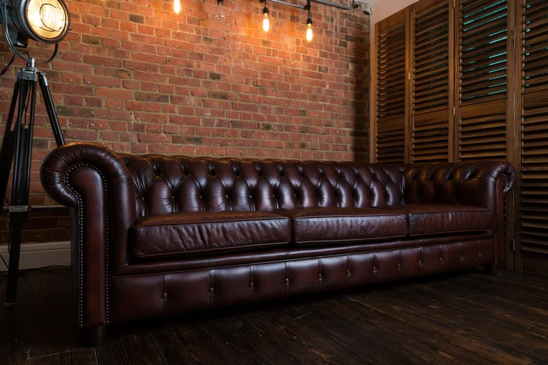 Dark brown tufted chesterfield leather sofa against exposed brick wall in industrial-style interior