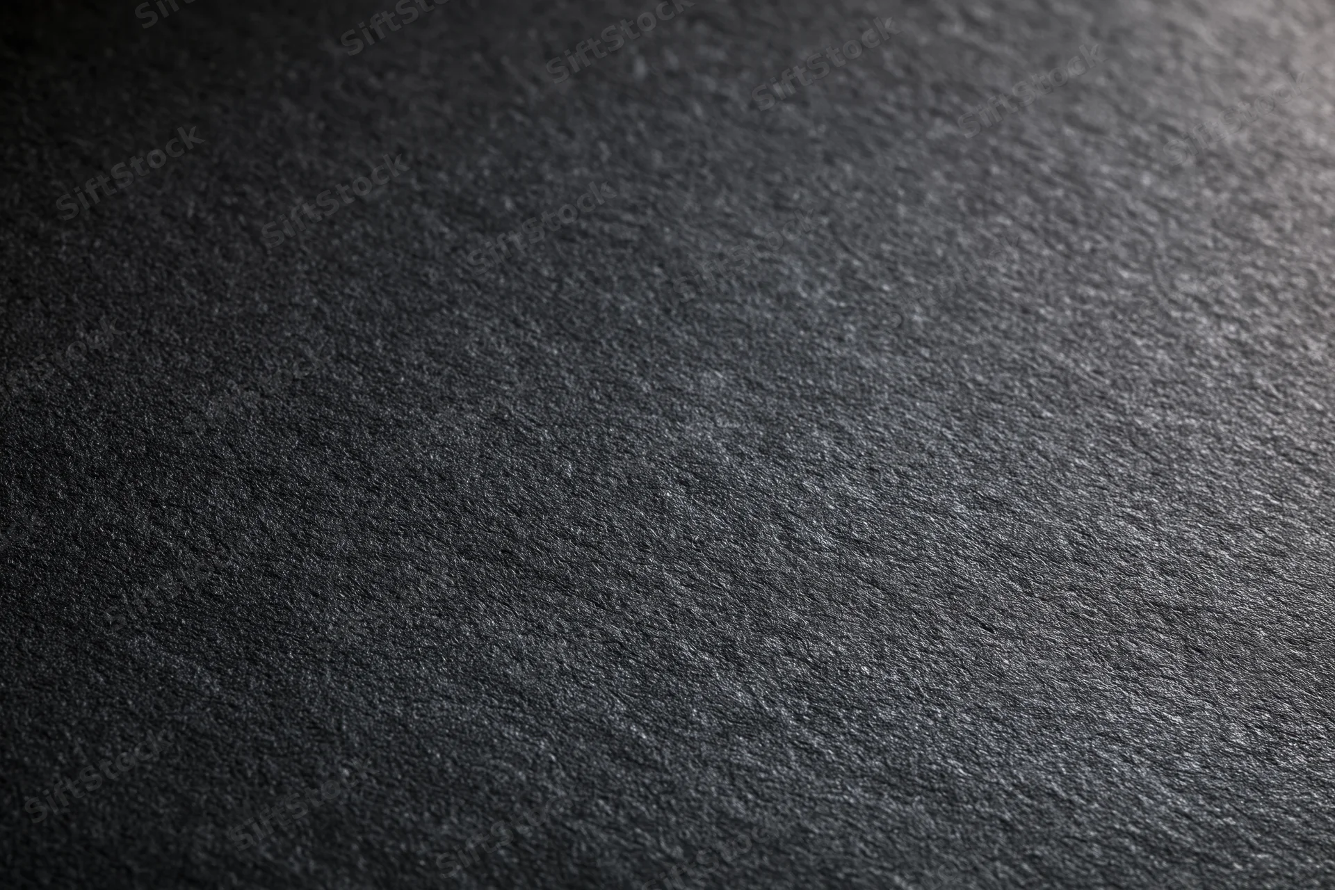 Dark charcoal matte surface filling the frame with textured grain and subtle light gradient