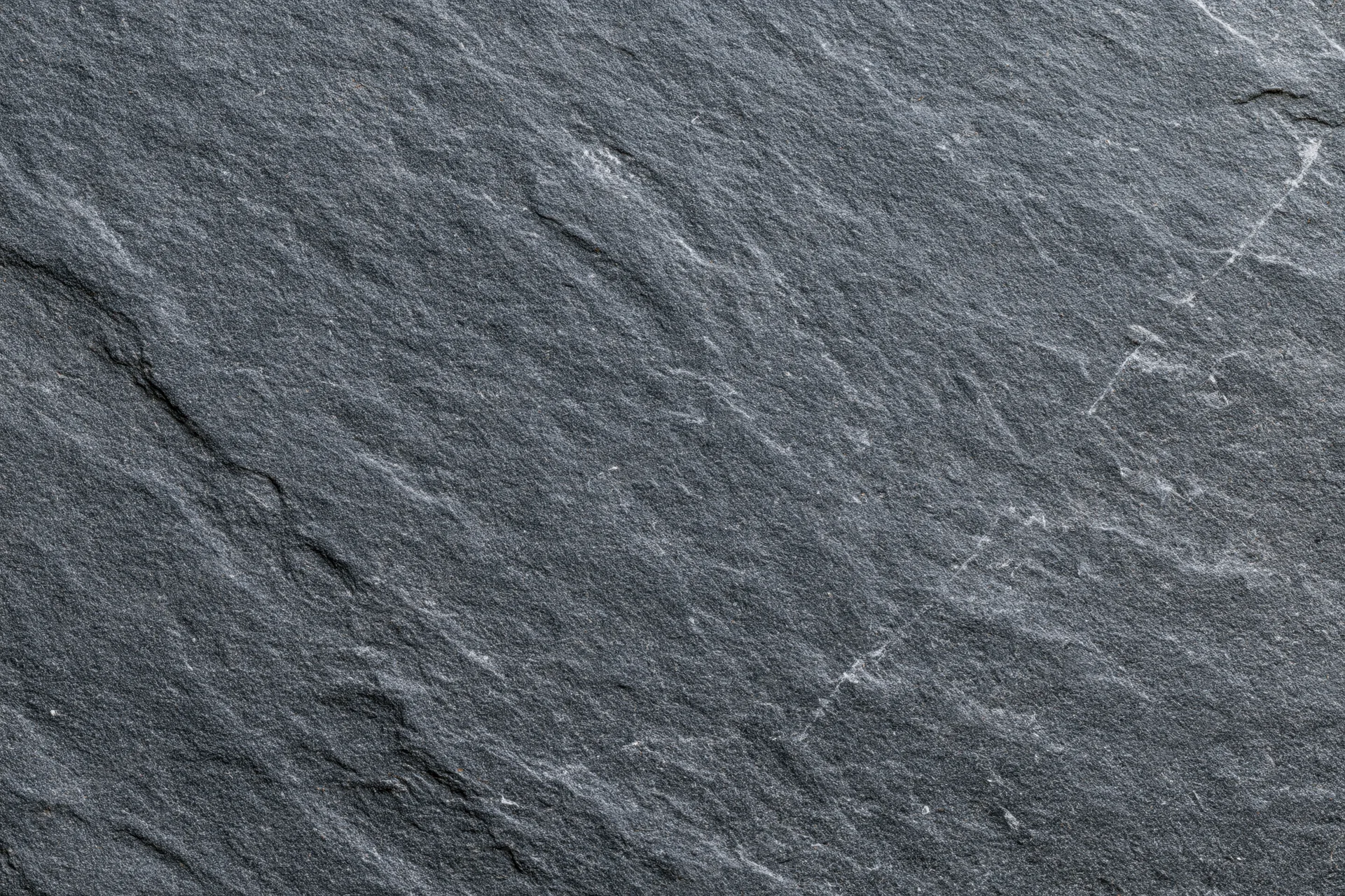Dark grey slate stone surface filling the frame with natural texture and cracks