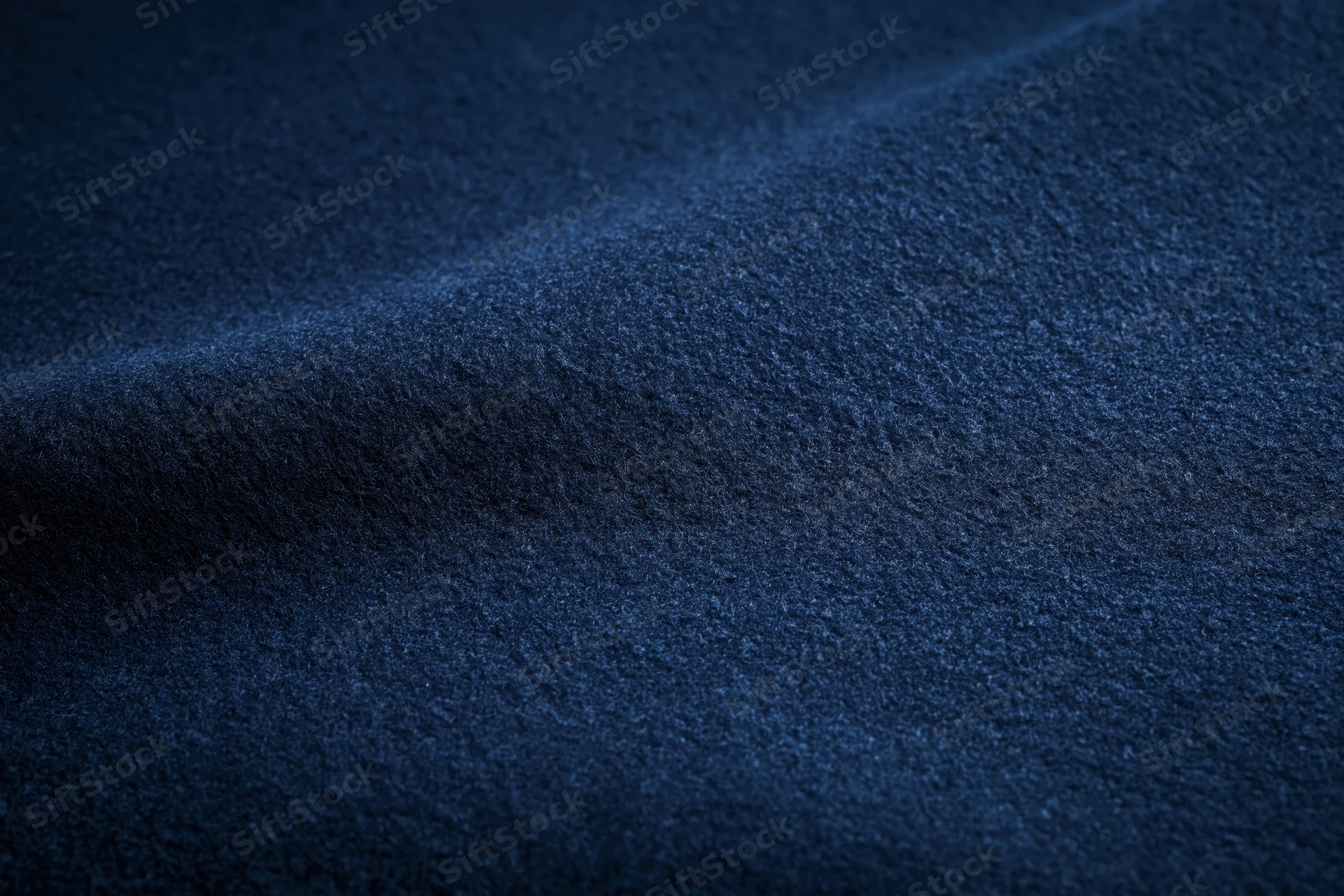 Closeup of deep navy blue textured fabric surface with folds and waves