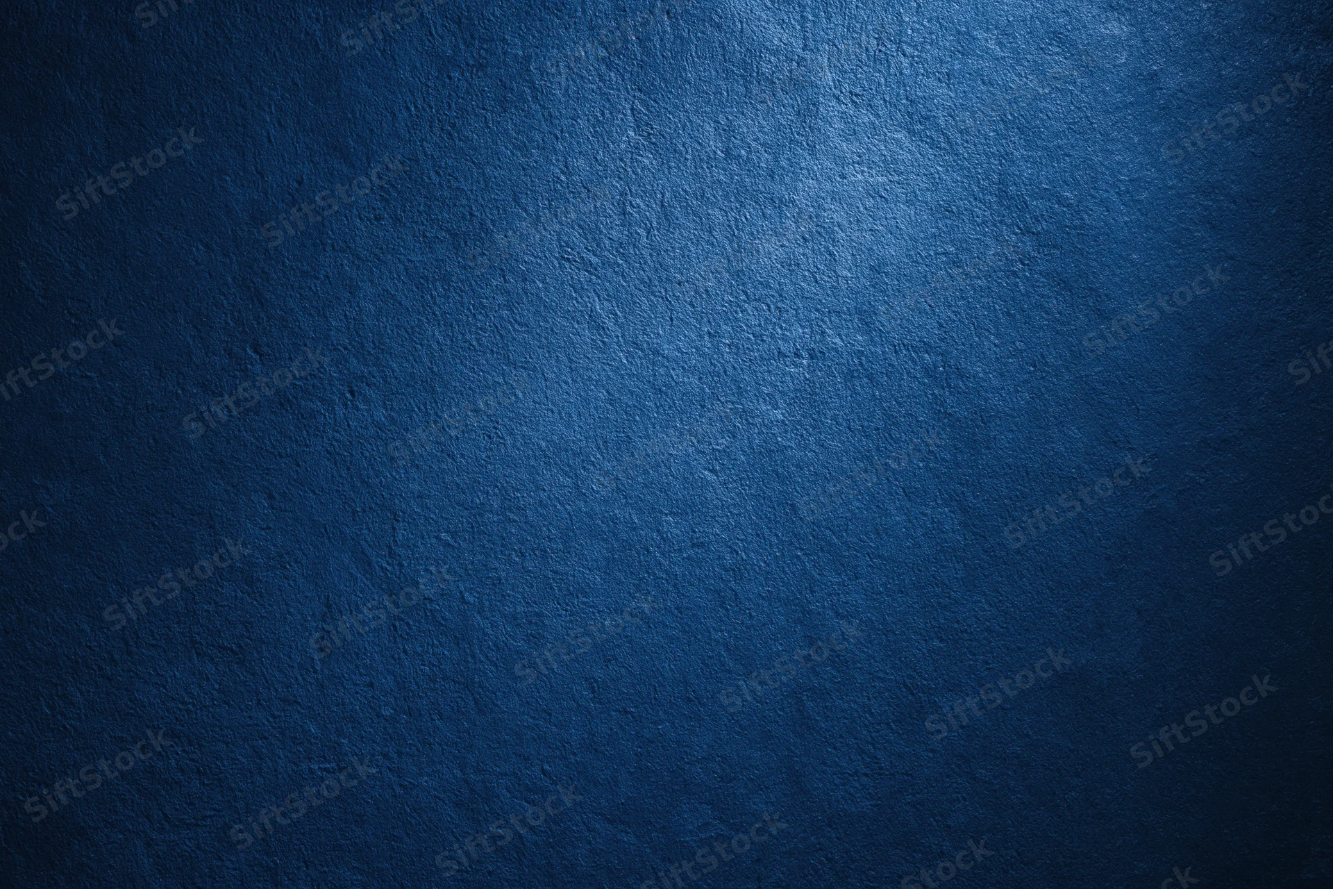 Closeup of a textured navy blue wall surface with light gradient and shadowed edges