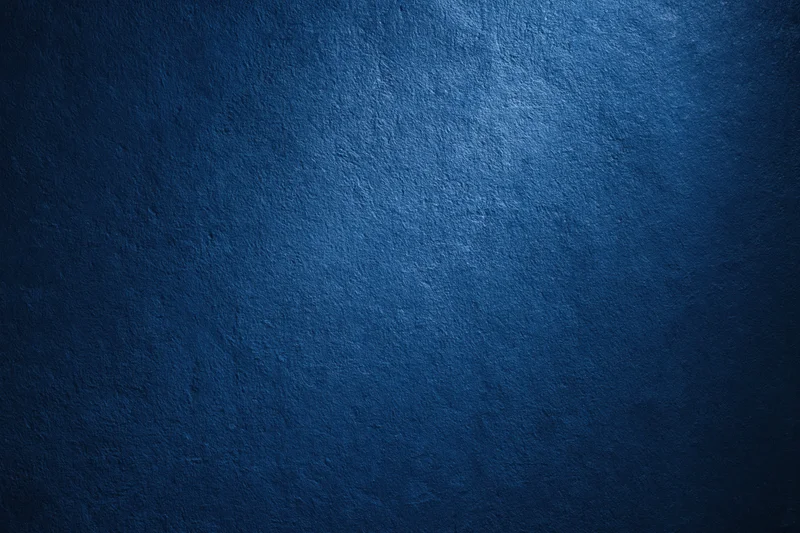 Closeup of a textured navy blue wall surface with light gradient and shadowed edges