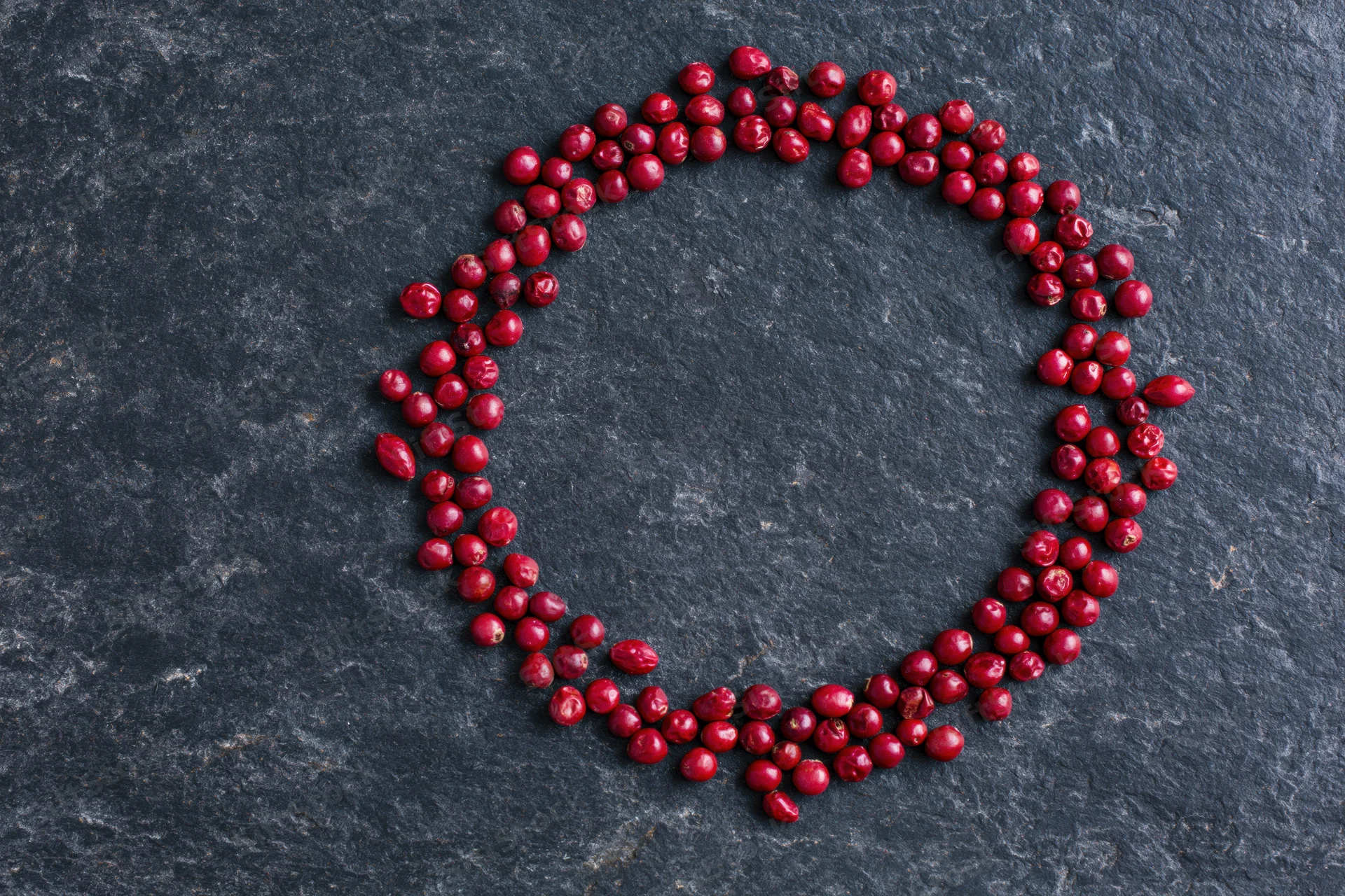 Dried red peppercorns arranged in a loose circular frame on dark slate surface
