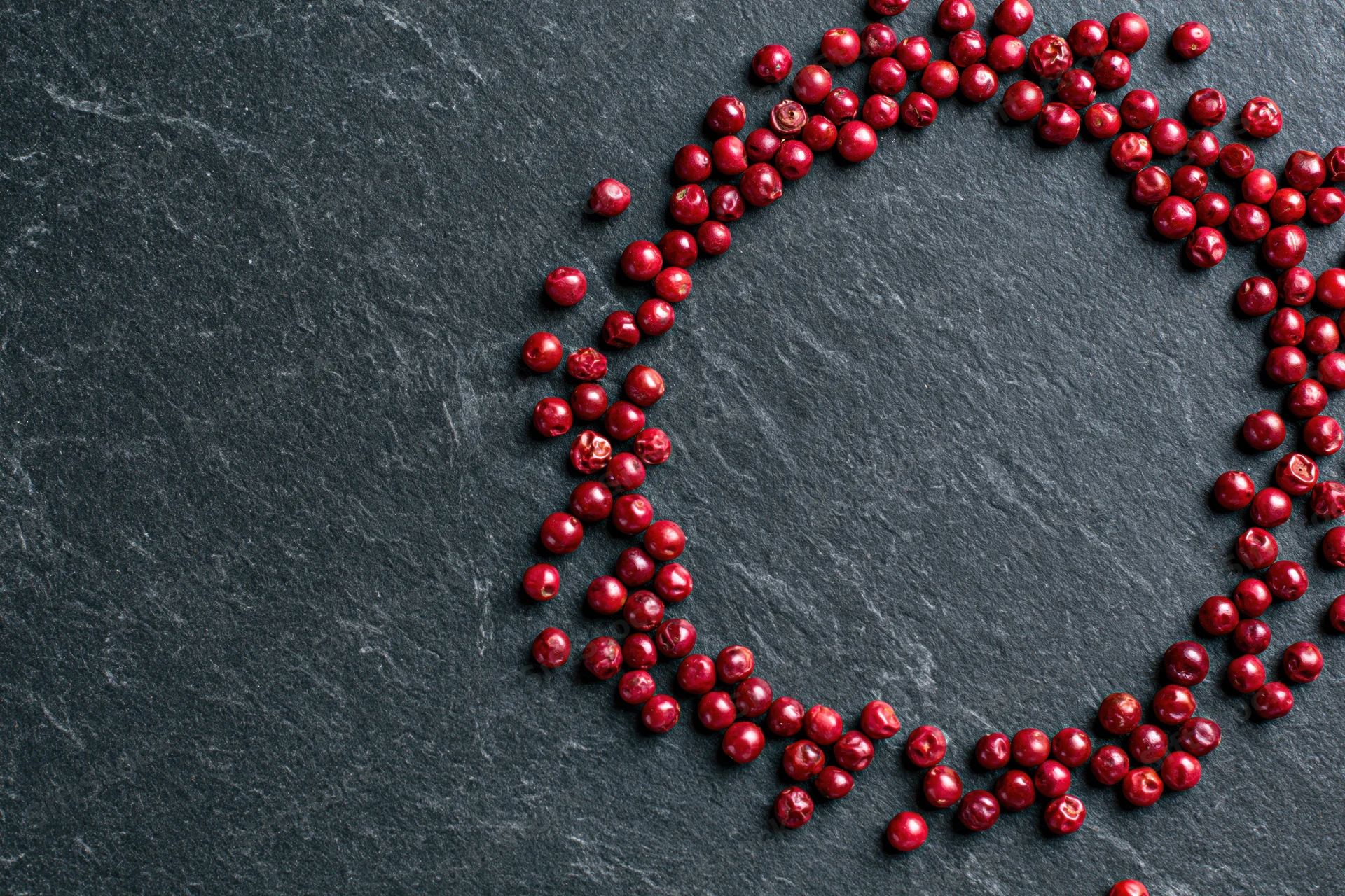 Dried red peppercorns arranged in a loose circular frame on dark slate surface