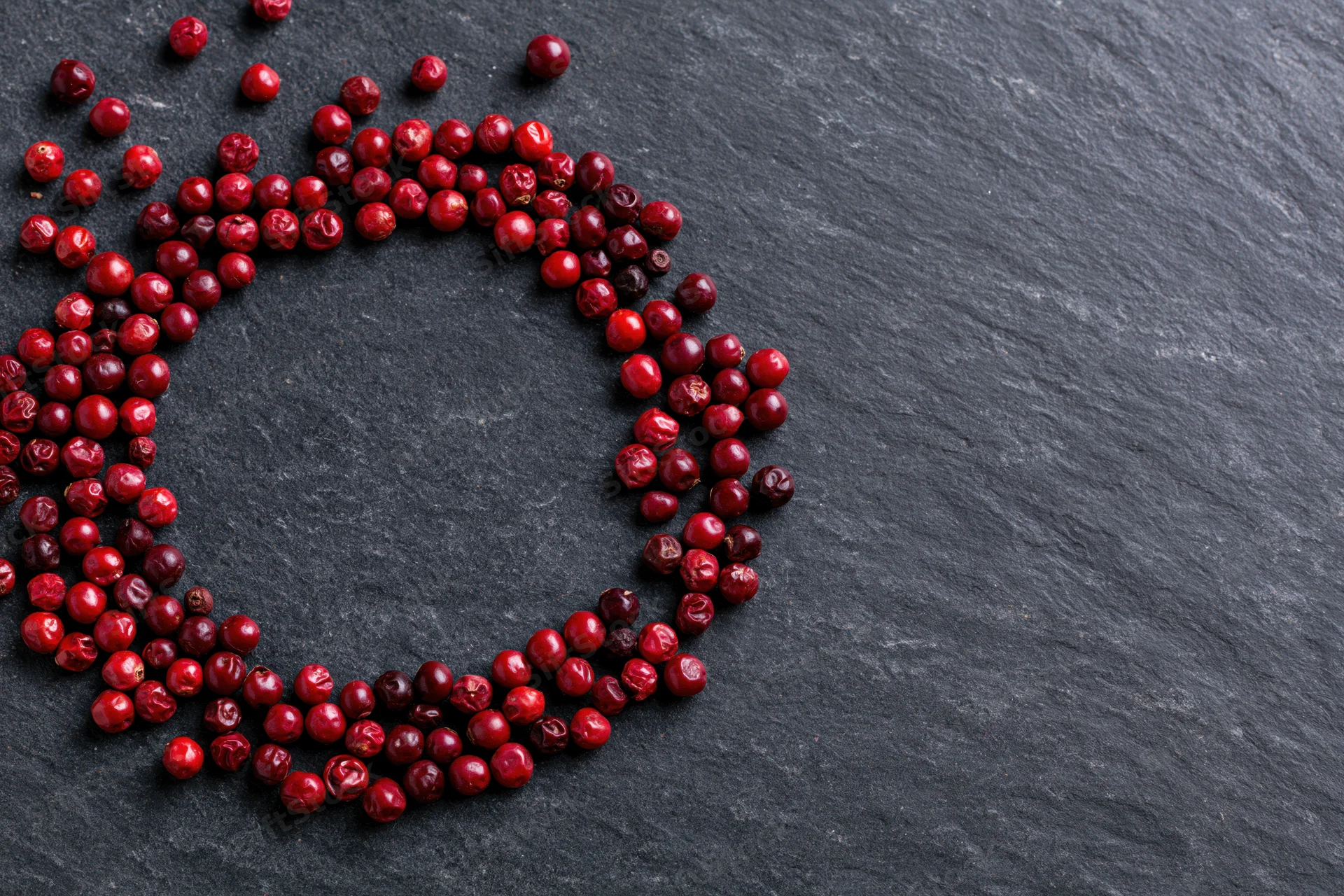 Dried red peppercorns arranged in a loose circular frame on a dark slate surface