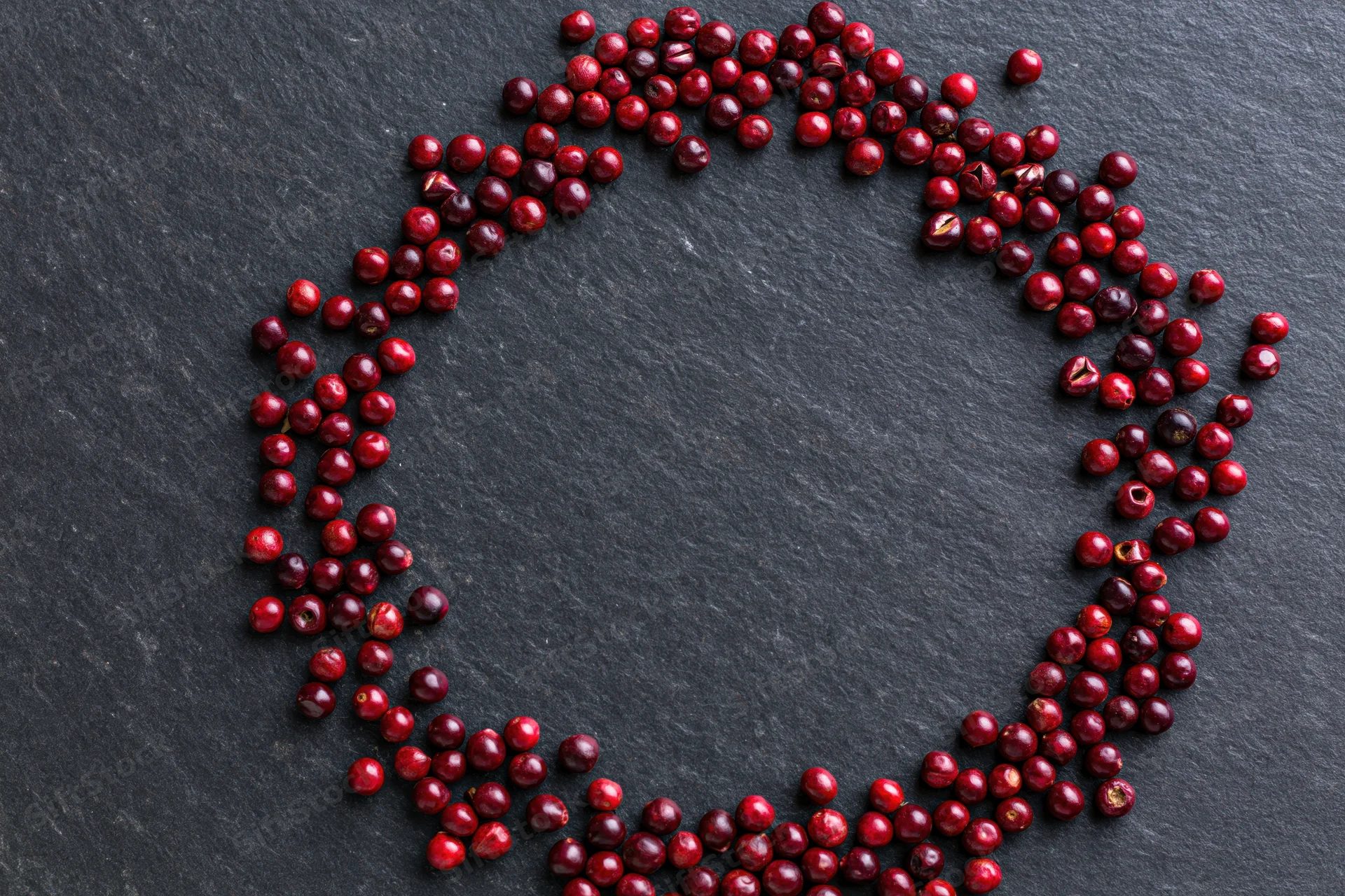 Dried red peppercorns arranged in a loose circular frame on dark slate surface