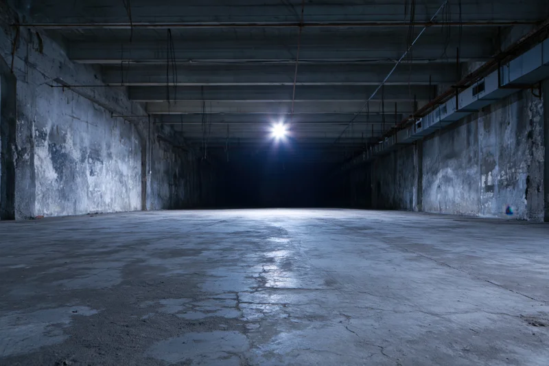 Empty abandoned industrial warehouse interior with single light source at far end