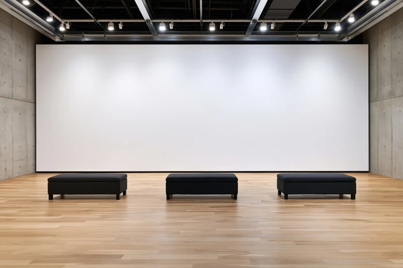 Empty contemporary art gallery interior with large blank white wall and three black benches on wooden floor
