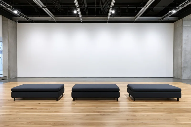Three black benches arranged in a row in an empty contemporary art gallery with white walls and wooden floor