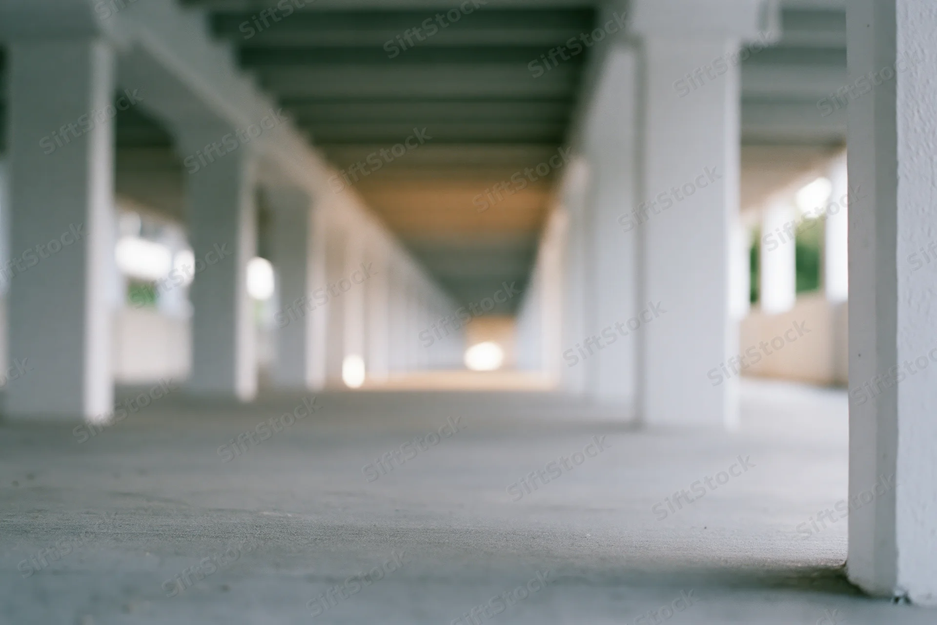 Low-angle view of a covered concrete corridor with repeating white pillars receding into the distance