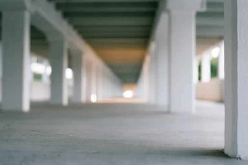 Low-angle view of a covered concrete corridor with repeating white pillars receding into the distance