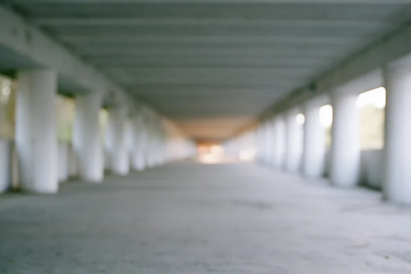 Empty concrete underpass corridor with repeating pillars receding into soft light