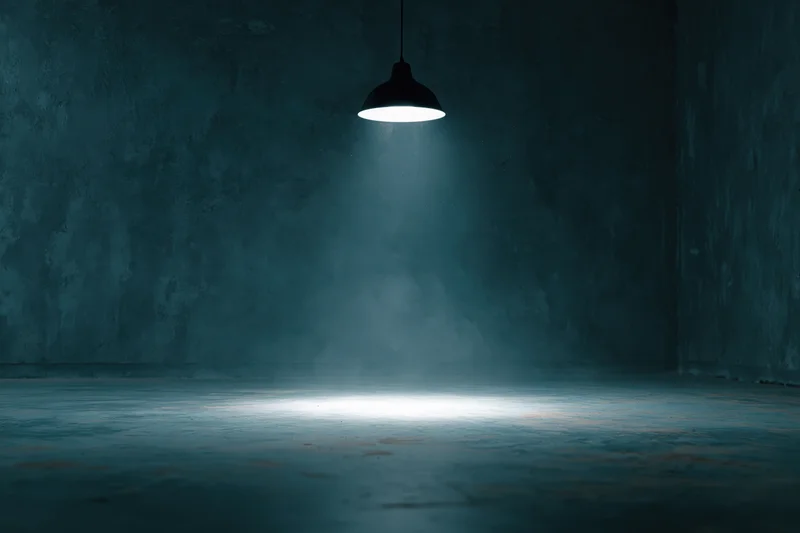Single pendant spotlight casting a beam of light on a concrete floor in a dark empty room